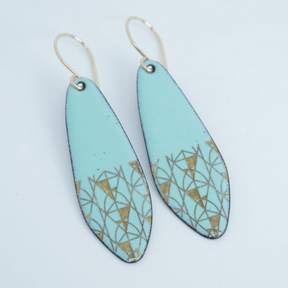A pair of seafoam green teardrop shaped earrings with gold geometric accents, suspended from thin gold hooks on a white background