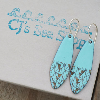 A pair of seafoam green teardrop shaped earrings with gold geometric accents, suspended from thin gold hooks on a gift box
