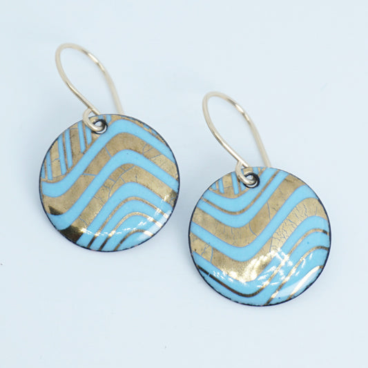 A pair of round drop earrings with light blue and gold wavy patterned enamel and gold-tone fishhook wires, shown on a white background
