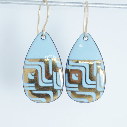 A pair of teardrop-shaped dangle earrings with a light blue enamel background, featuring a metallic geometric pattern, hanging from thin gold hooks.