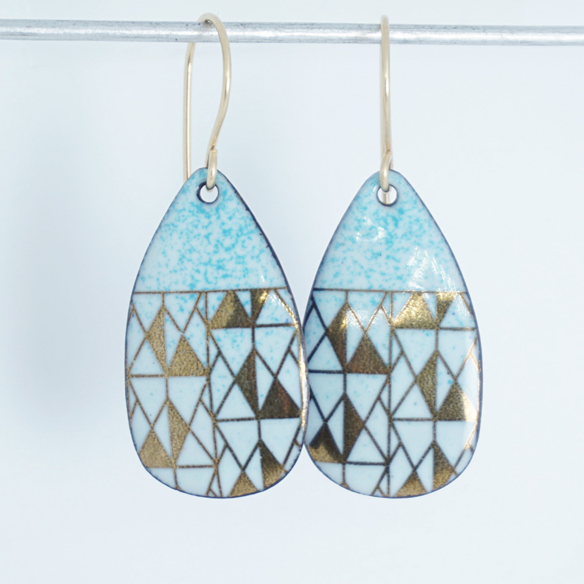 A pair of teardrop-shaped dangle earrings with seafoam green enamel and gold geometric pattern, against a white background