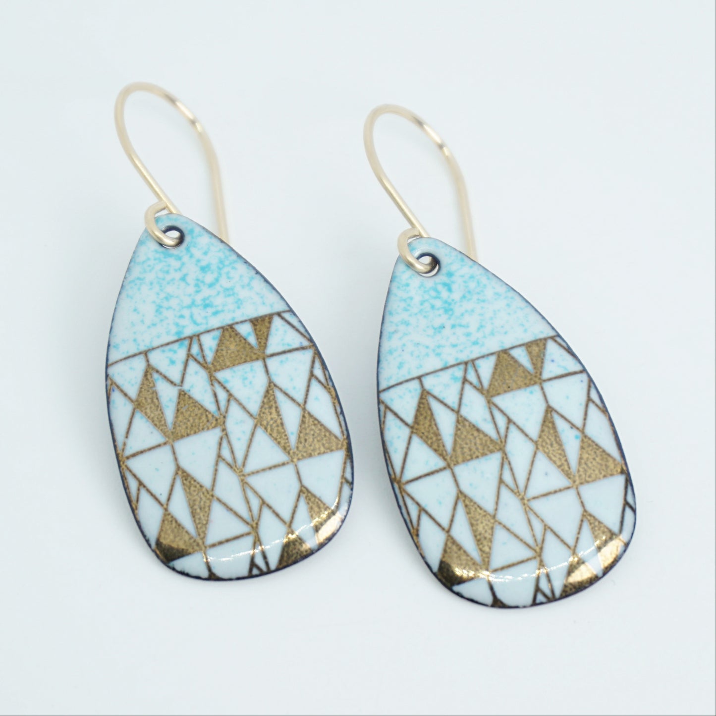 A pair of teardrop-shaped dangle earrings with seafoam green enamel and gold geometric pattern, against a white background