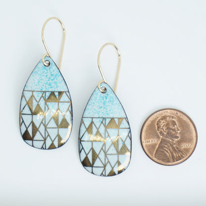 A pair of teardrop-shaped dangle earrings with seafoam green enamel and gold geometric pattern, next to a penny for scale, against a white background
