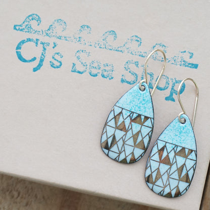 A pair of teardrop-shaped dangle earrings with seafoam green enamel and gold geometric pattern, displayed on a gift box