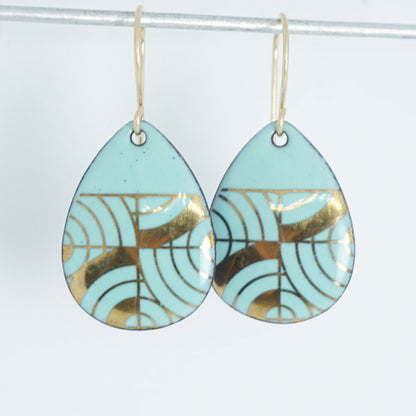 A pair of teardrop-shaped dangle earrings with seafoam green enamel and gold geometric pattern, against a white background