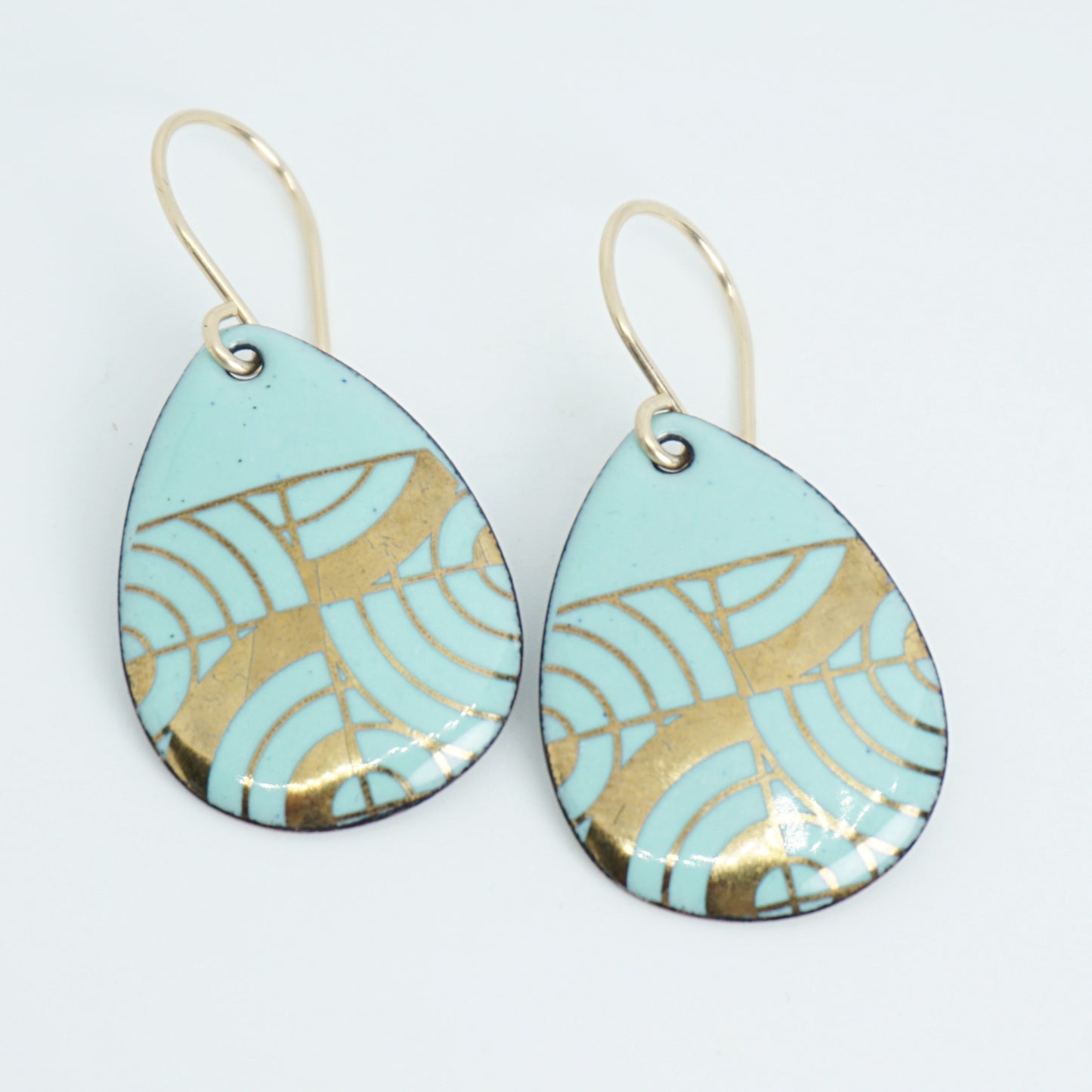 A pair of teardrop-shaped dangle earrings with seafoam green enamel and gold geometric pattern, against a white background