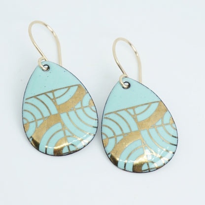 A pair of teardrop-shaped dangle earrings with seafoam green enamel and gold geometric pattern, against a white background