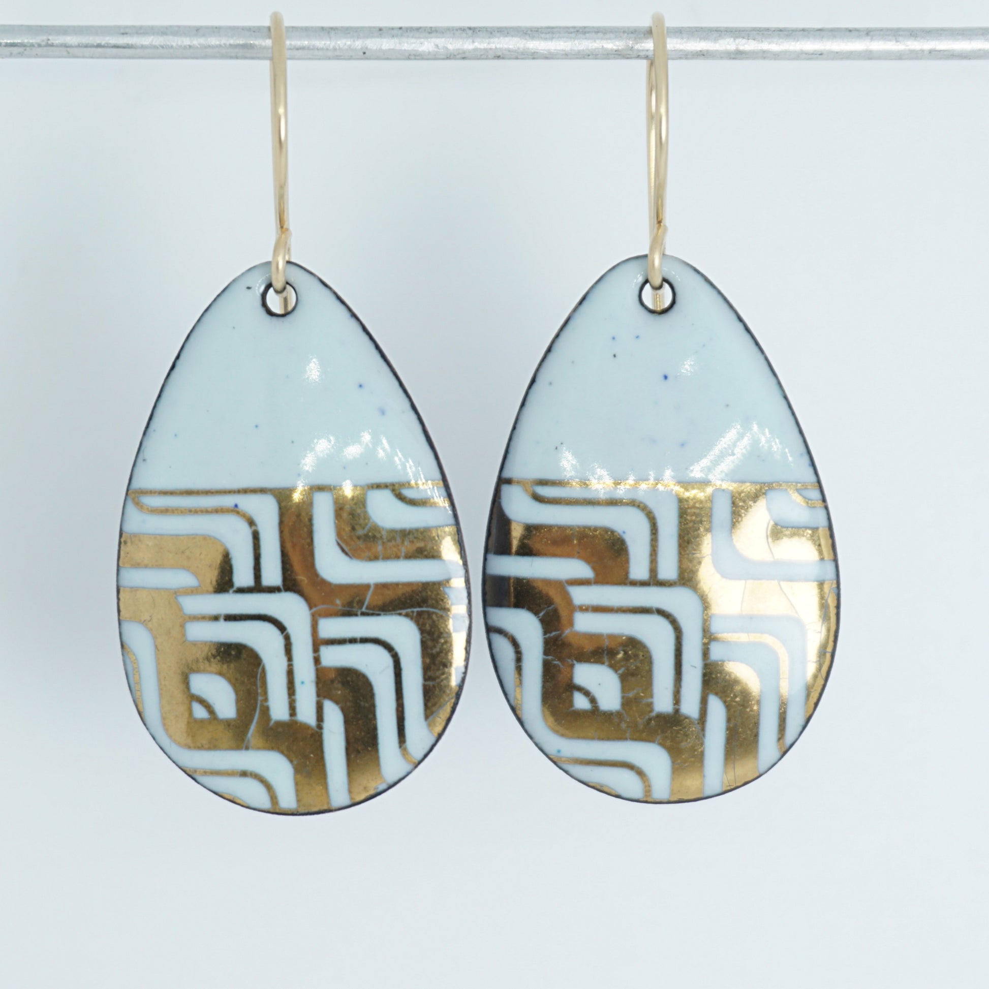 A pair of teardrop-shaped dangle earrings with seafoam green enamel and gold geometric pattern, against a white background