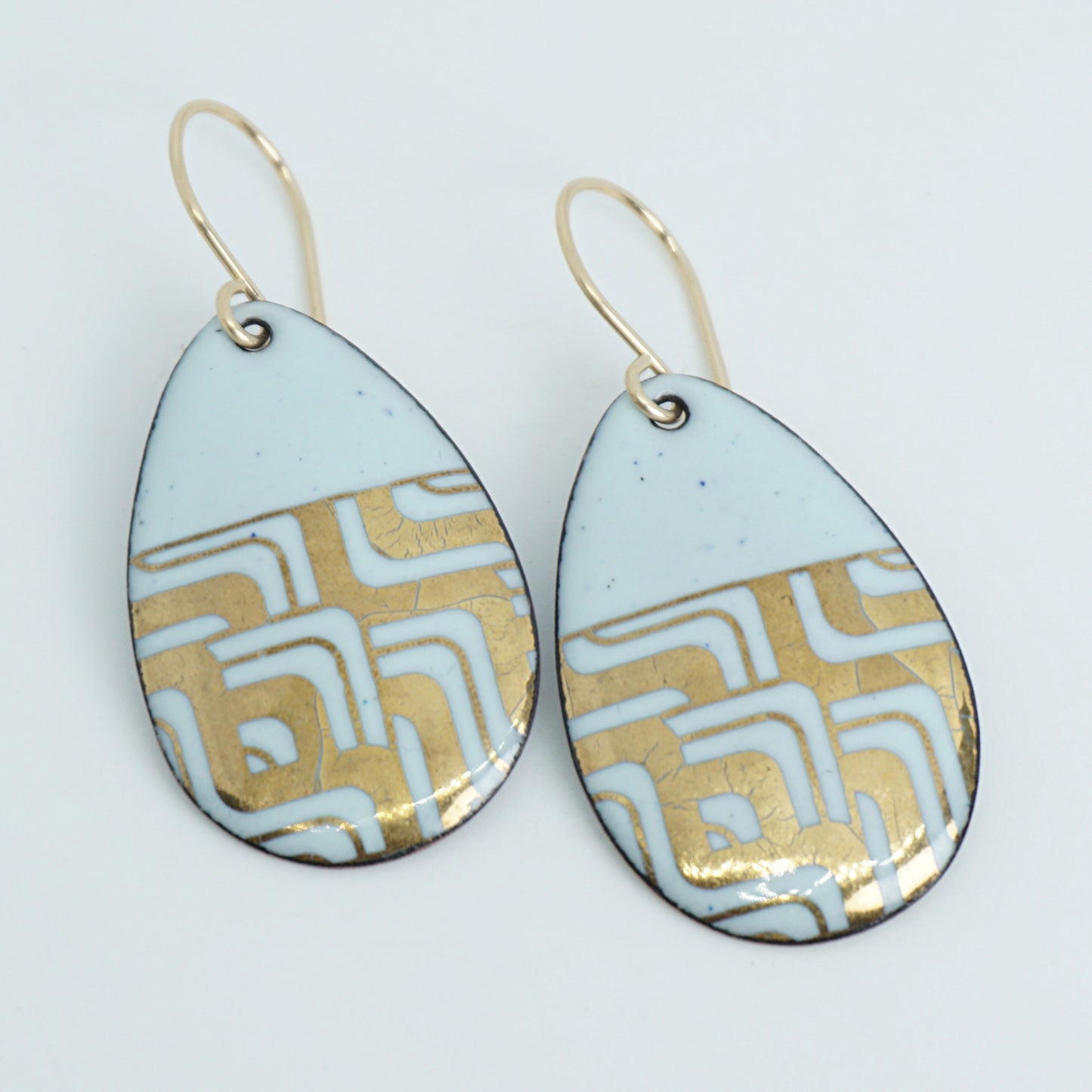 A pair of teardrop-shaped dangle earrings with seafoam green enamel and gold geometric pattern, against a white background
