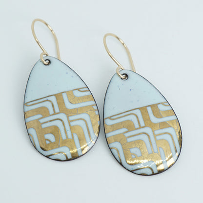 A pair of teardrop-shaped dangle earrings with seafoam green enamel and gold geometric pattern, against a white background