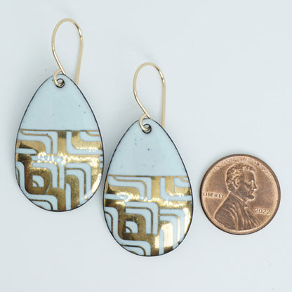 A pair of teardrop-shaped dangle earrings with seafoam green enamel and gold geometric pattern, next to a penny for scale, against a white background