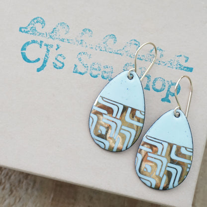 A pair of teardrop-shaped dangle earrings with seafoam green enamel and gold geometric pattern, displayed on a gift box