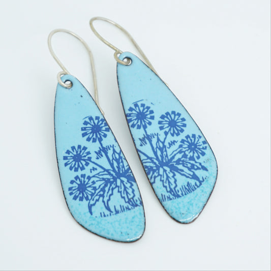 A pair of light blue teardrop earrings with blue floral dandelion designs, against a white background