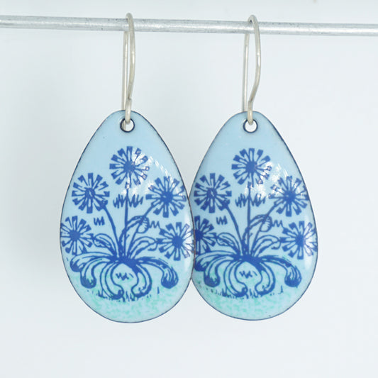 A pair of light blue teardrop earrings with blue floral dandelion designs, against a white background