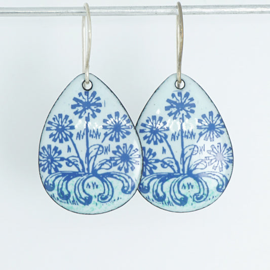 A pair of light seafoam green teardrop earrings with blue floral dandelion designs, against a white background