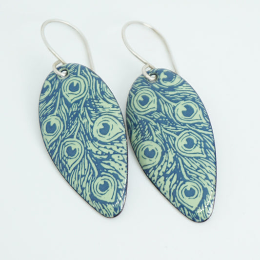 A pair of teardrop-shaped drop earrings with a blue and light green peacock feather pattern, suspended from silver wire hooks on a plain white background.