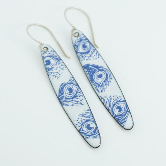 A pair of long dangle earrings with a blue peacock feather pattern on a white background, suspended from silver fishhook wires.