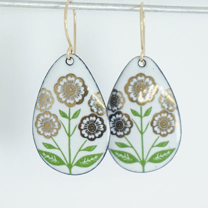 White teardrop-shaped dangle earrings, with gold flowers on green stems dangling from gold hooks, against a white background