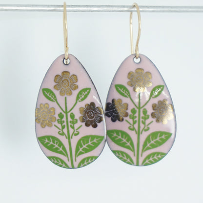 Pink teardrop-shaped dangle earrings, with gold flowers on green stems dangling from gold hooks, against a white background