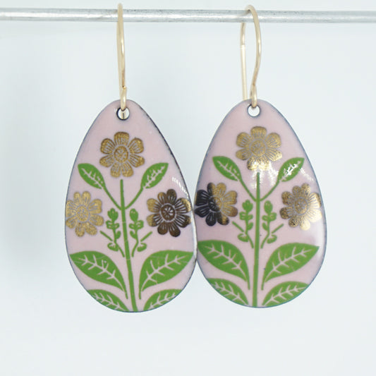 Pink teardrop-shaped dangle earrings, with gold flowers on green stems dangling from gold hooks, against a white background