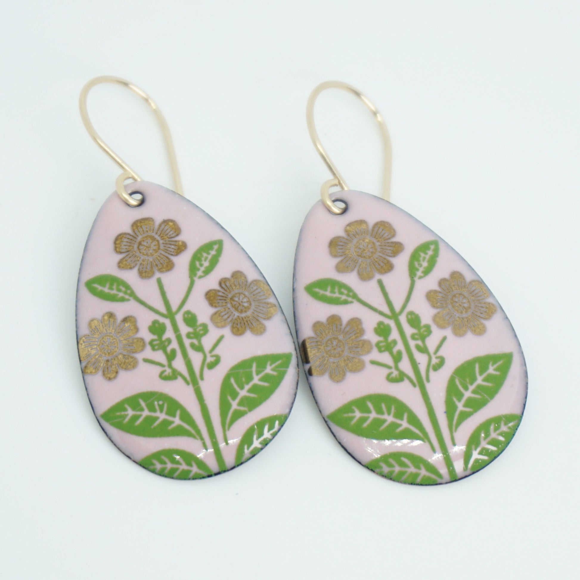 Pink teardrop-shaped dangle earrings, with gold flowers on green stems dangling from gold hooks, against a white background
