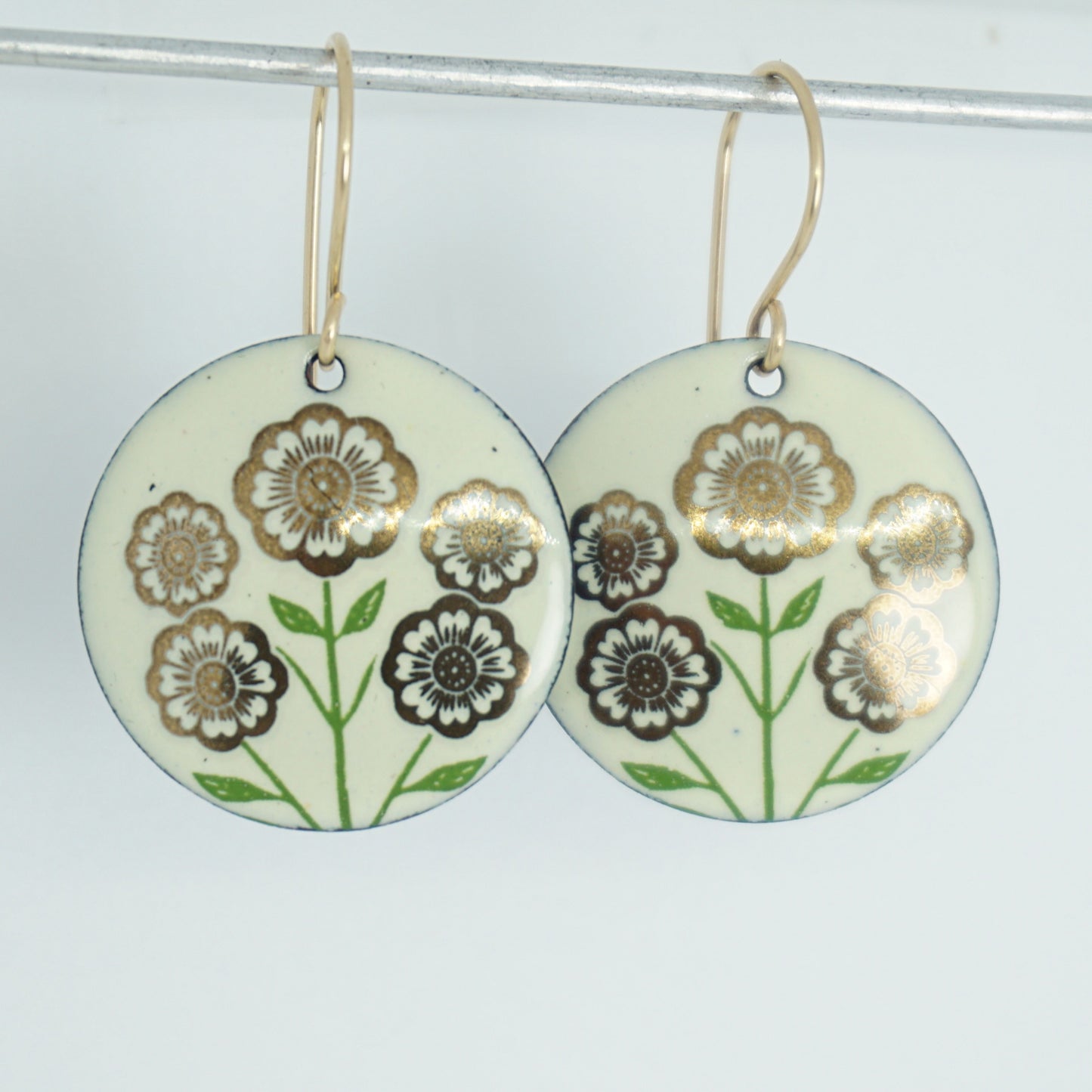Light yellow disc-shaped dangle earrings, with gold flowers on green stems dangling from gold hooks, against a white background
