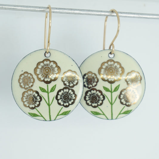 Light yellow disc-shaped dangle earrings, with gold flowers on green stems dangling from gold hooks, against a white background