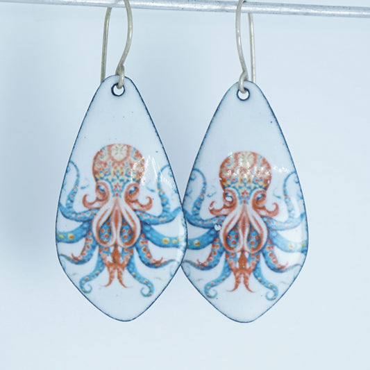 A pair of teardrop-shaped dangling earrings with a white background and a printed octopus design in blue and orange, hanging from thin metal hooks against a white backround