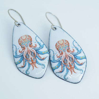 A pair of teardrop-shaped dangling earrings with silver fishhook wires. The glossy white enamel faces feature an octopus design in coral orange and light blue