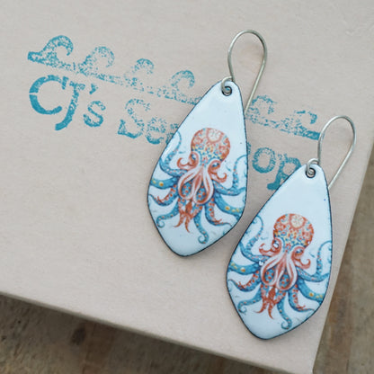 A pair of teardrop-shaped earrings with octopus designs, displayed on a gift box