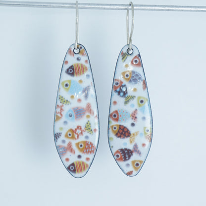 A pair of teardrop-shaped dangling earrings with a white background and a colorful pattern of small fish, hanging from silver hooks against a white background.