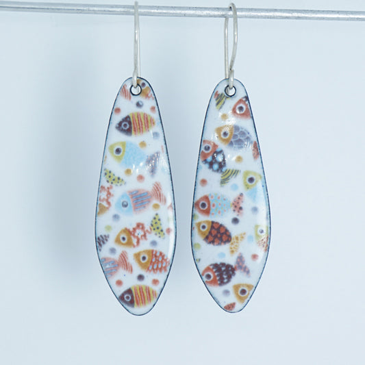 A pair of teardrop-shaped dangling earrings with a white background and a colorful pattern of small fish, hanging from silver hooks against a white background.