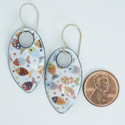 a pair of teardrop-shaped dangling earrings with a colorful fish pattern on a white background, shown next to a penny for scale