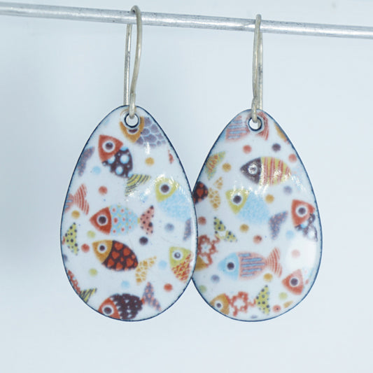a pair of teardrop shaped white enamel earrings with a colorful fish print, against a white background