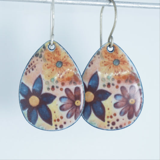 A pair of teardrop-shaped dangling earrings with a colorful floral pattern on a light background, hanging from silver fishhook wires.