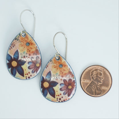 Teardrop-shaped dangling earrings with a colorful floral pattern on a light background, shown next to a penny for scale on a plain white surface.