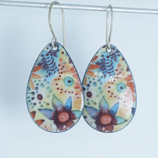 A pair of teardrop-shaped dangling earrings with a colorful floral pattern, hanging from silver fishhook wires against a plain light background.