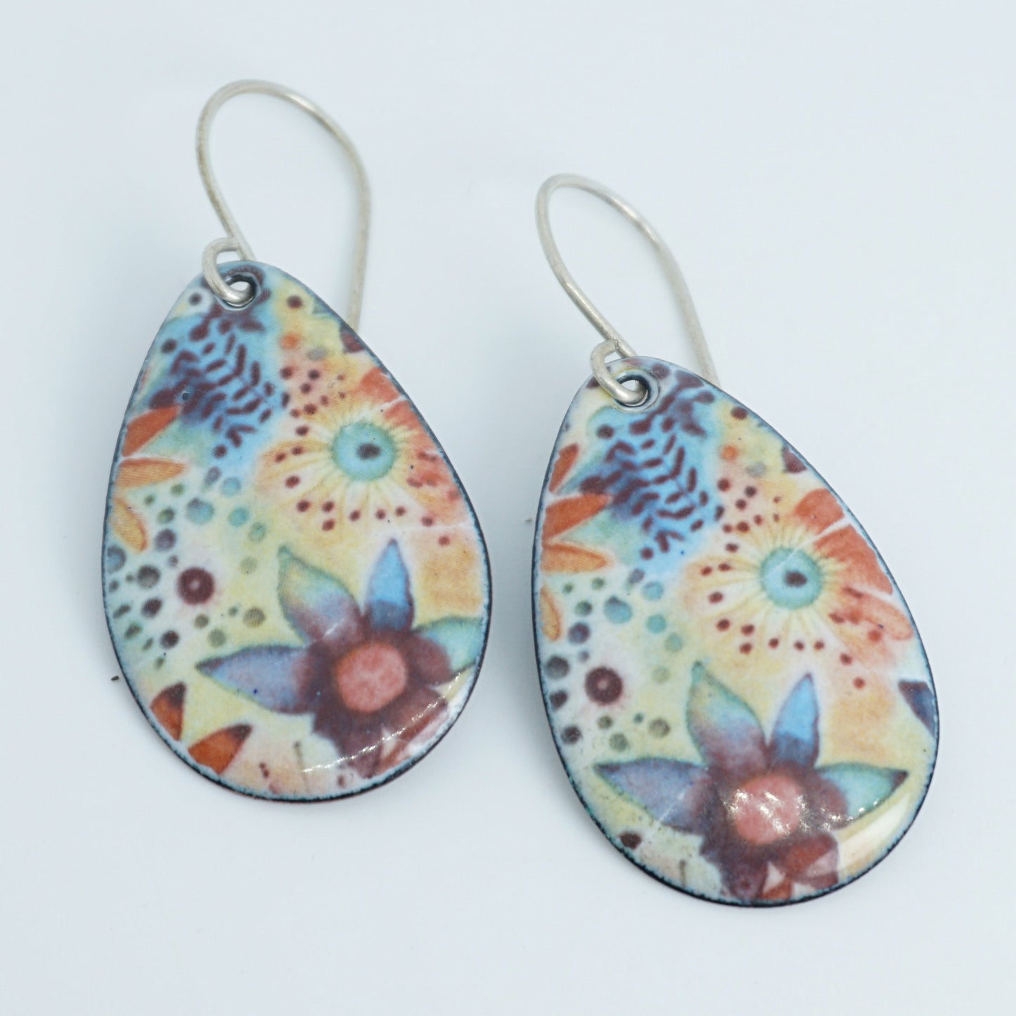 A pair of teardrop-shaped drop earrings with a colorful floral pattern on a light background, hanging from silver fishhook wires.