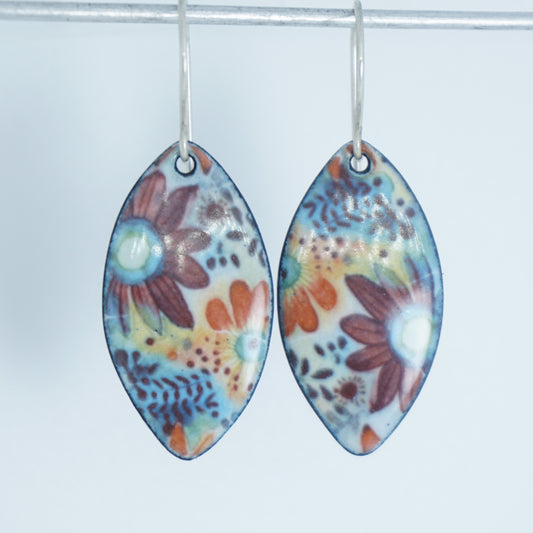 A pair of marquise-shaped dangling earrings with a colorful floral pattern, hanging from silver hooks against a white background