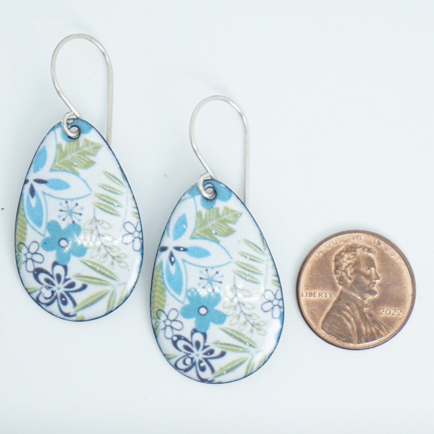Teardrop-shaped dangle earrings with a blue, green, and white floral pattern, shown next to a US penny for scale on a white background.