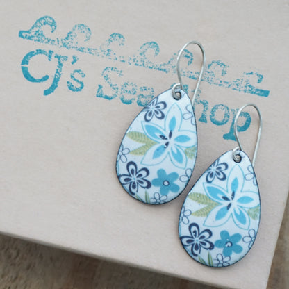 Teardrop-shaped floral earrings with blue, white, and green patterns on a gift box