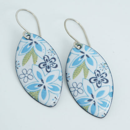 A pair of marquis-shaped drop earrings with a white enamel background decorated with blue and green floral patterns, suspended from silver-tone wire hooks.