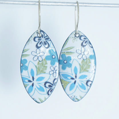 A pair of dangling marquise-shaped earrings with a white background and a purple, light blue, and green floral pattern, hanging from silver hooks against a white background.