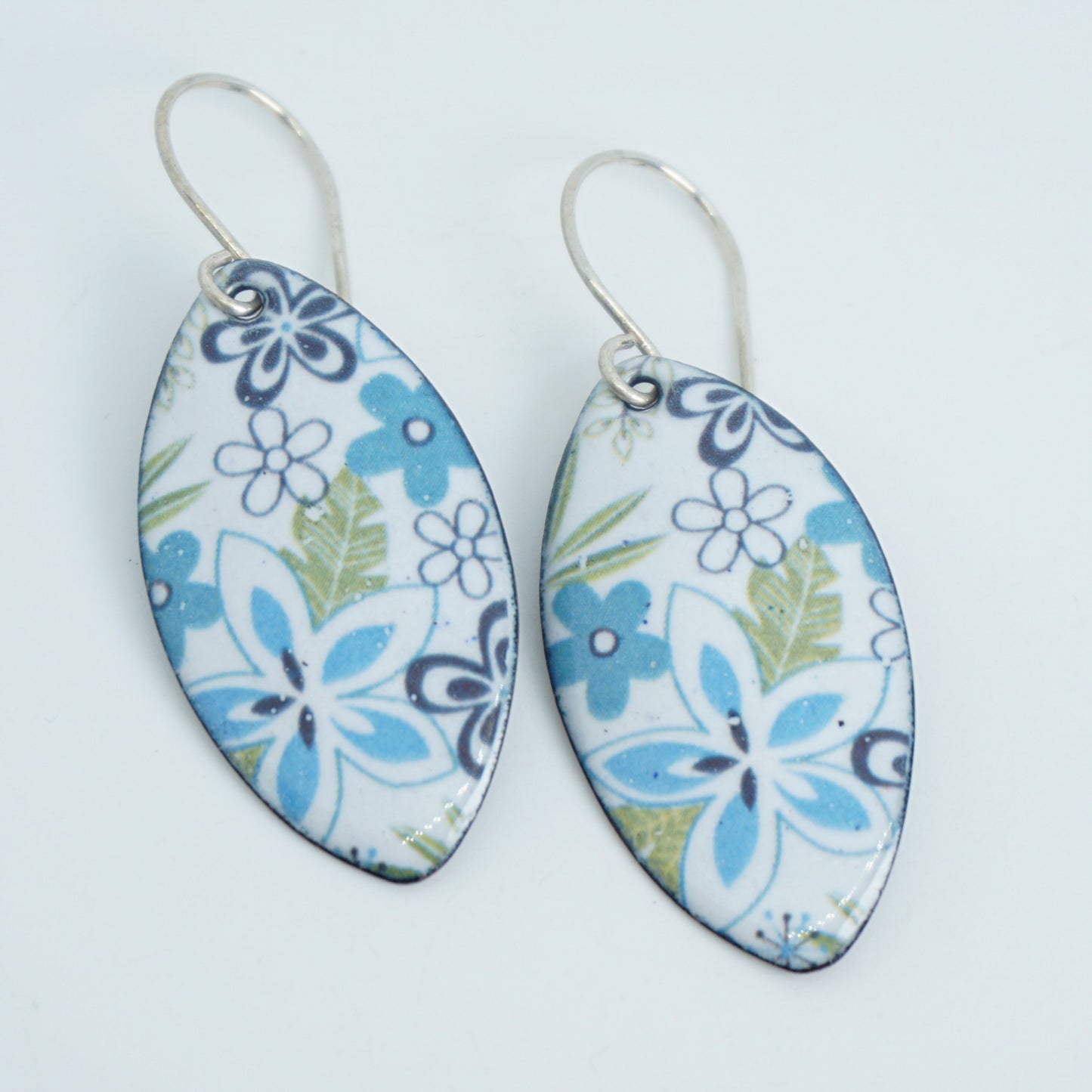 A pair of marquis-shaped dangling earrings with a white background and a blue, purple, and green floral pattern, suspended from silver fishhook wires on a white background.