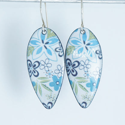 A pair of teardrop-shaped white enamel pendants decorated with a blue, purple, and green floral pattern, hanging against a plain white background.