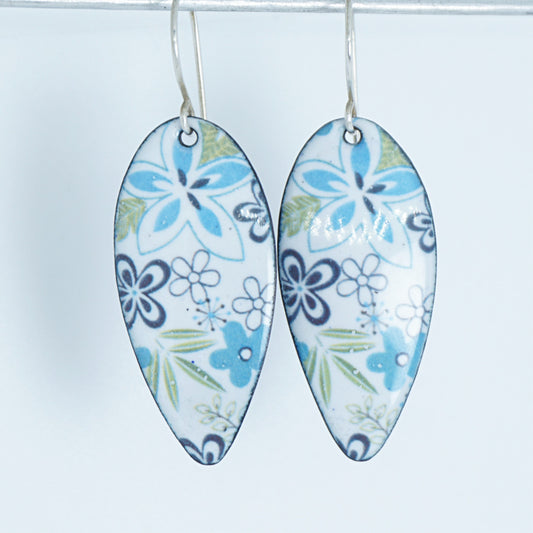 A pair of teardrop-shaped white enamel pendants decorated with a blue, purple, and green floral pattern, hanging against a plain white background.