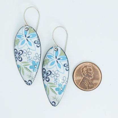 A pair of teardrop-shaped dangle earrings with a blue, green, and purple floral pattern on a white background, shown next to a US penny for scale on a white background.