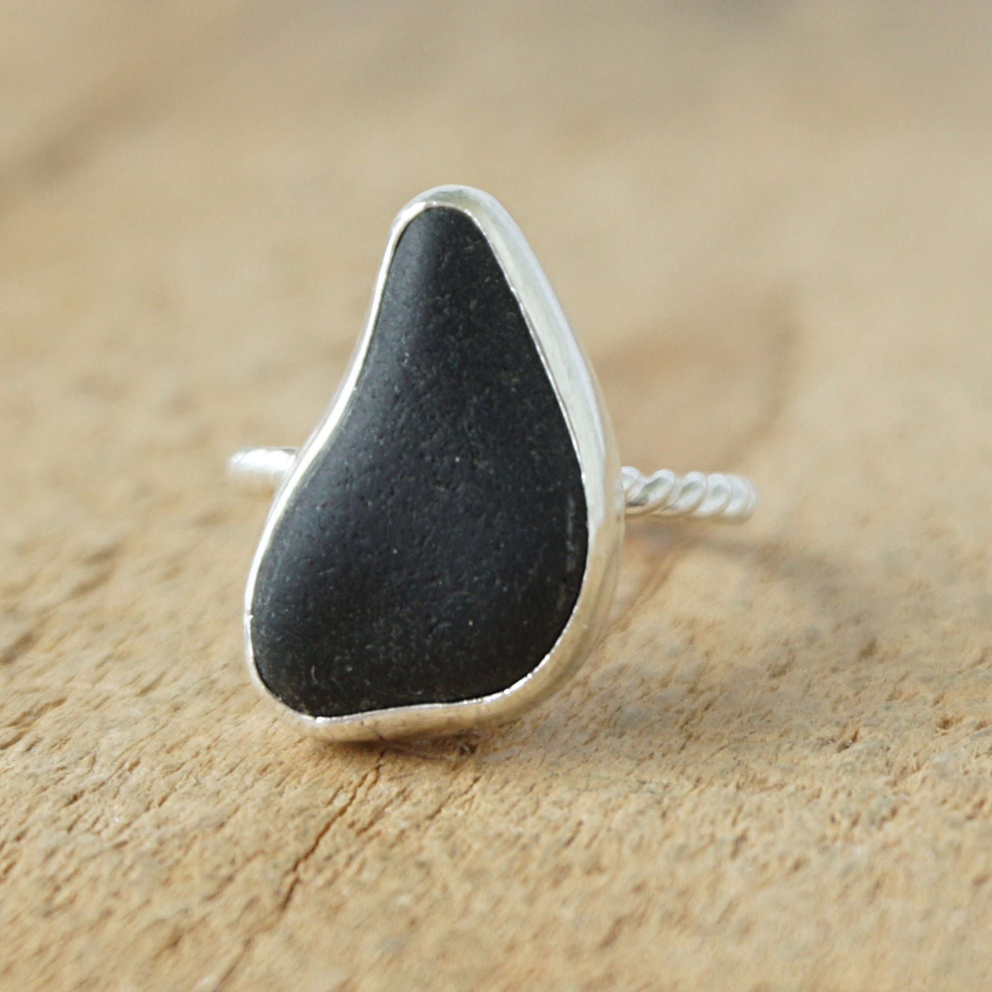 A sterling silver ring featuring teardrop-shaped black sea glass, on a textured light brown wood surface.