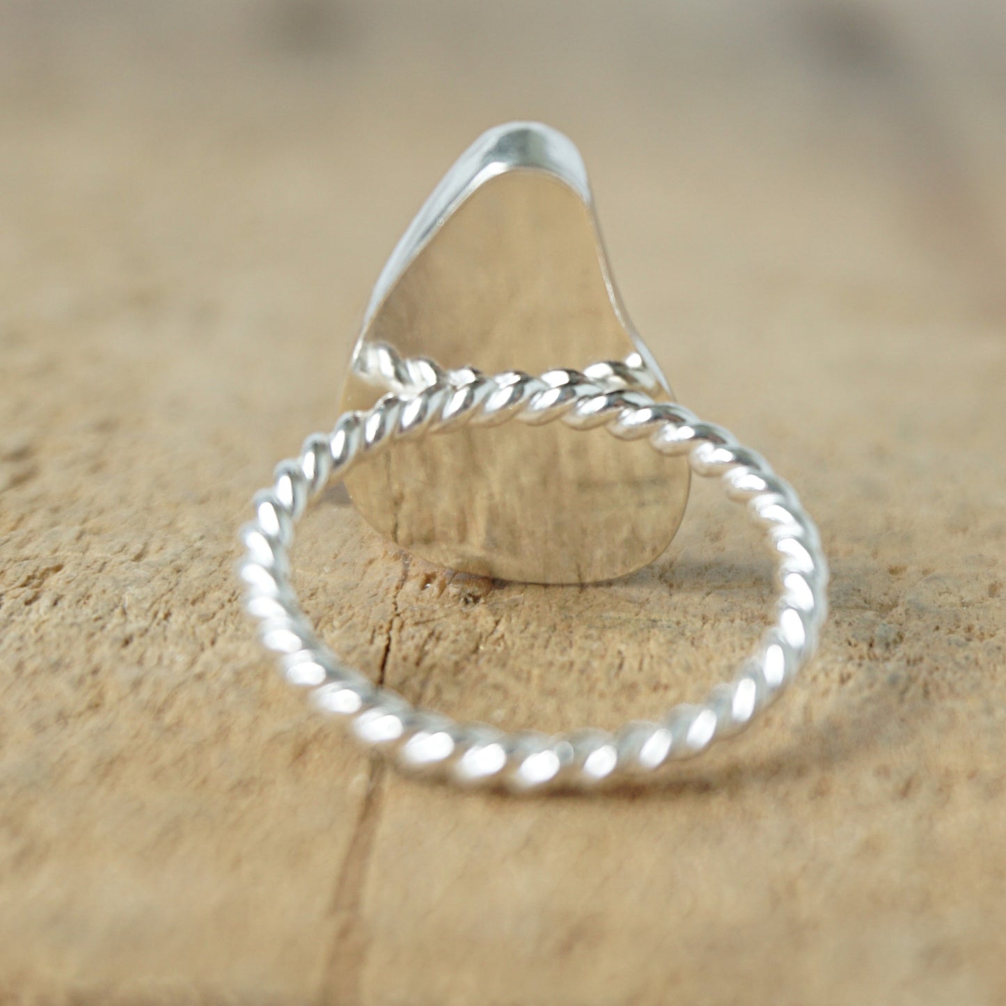 back view of A sterling silver ring featuring teardrop-shaped black sea glass, on a textured light brown wood surface.