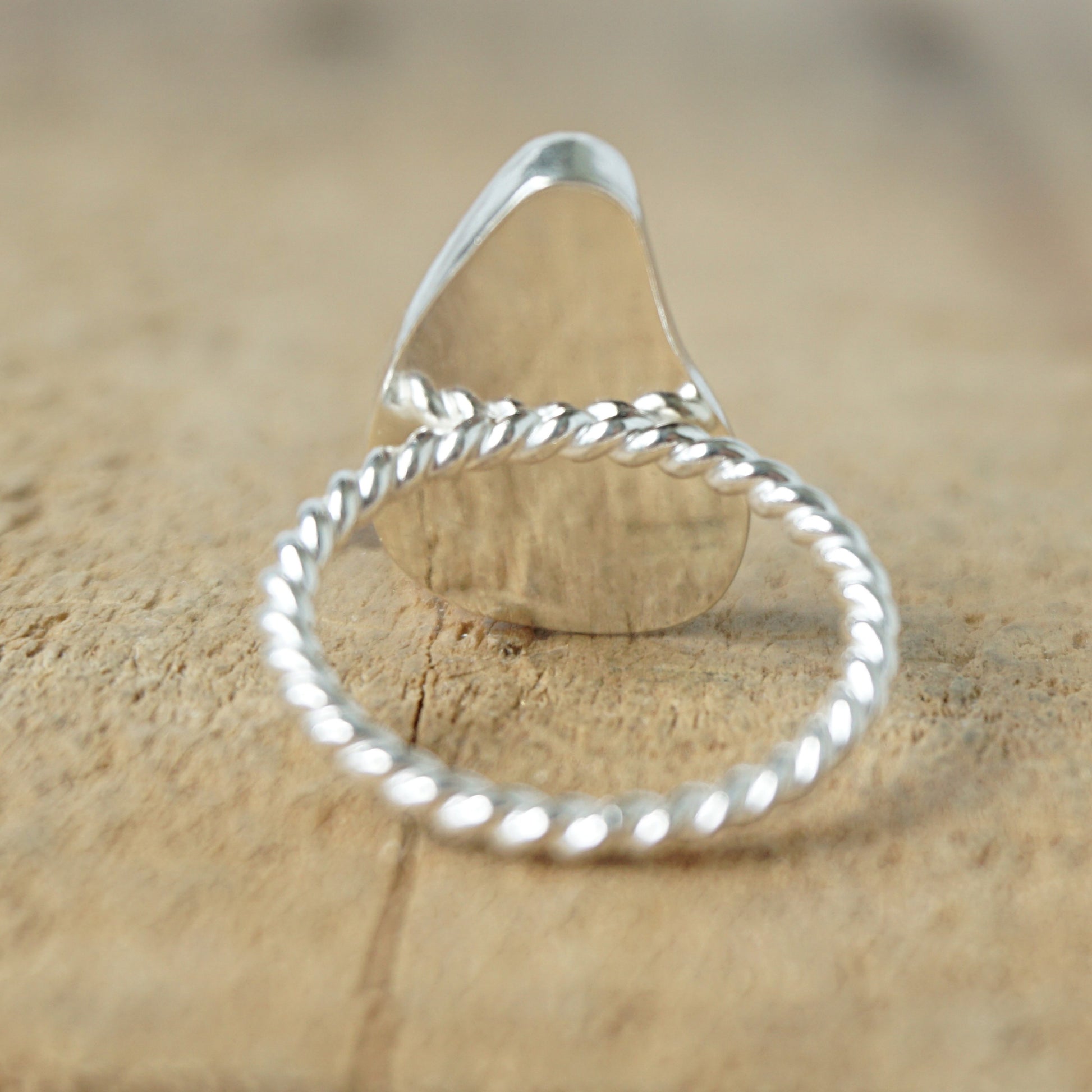 back view of A sterling silver ring featuring teardrop-shaped black sea glass, on a textured light brown wood surface.